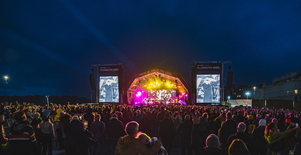 The stage to Plymouth Summer Sessions at night with members of the crowd at the front of the image